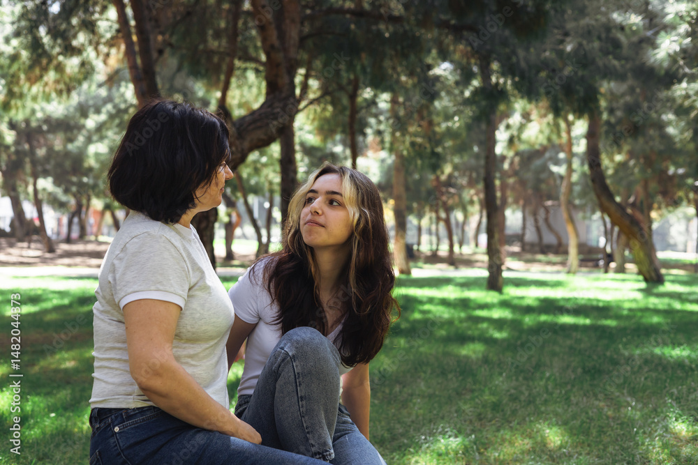 Fototapeta premium Two women sit closely together in a serene park setting