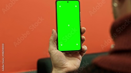 Man holding smartphone with green screen and tracking markers close up over shoulder view. Mobile phone mockup display chroma key space for application web template. Digital device usage