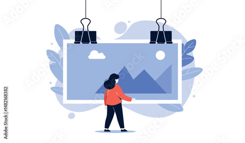 Person admiring framed mountain art in minimalist setting with leaves and clouds