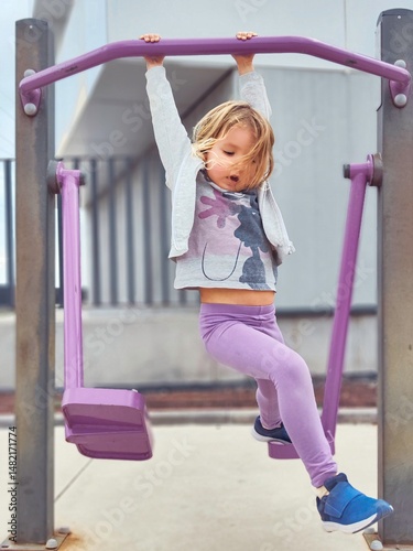 Little girl hanging from monkey bars at playground having fun