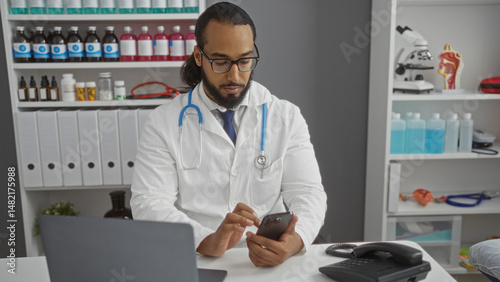 Wallpaper Mural Young man with beard in white coat using smartphone in clinic office surrounded by medical equipment and documents in professional indoor healthcare environment Torontodigital.ca