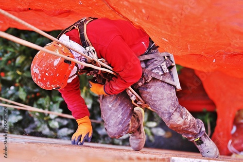 Obrero descolgado en rapel vertical en fachada con góndola, arnés, cuerda, casco, mosquetón, red y elementos de seguridad en altura para prevención de riesgo laboral