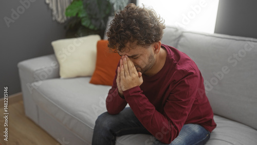 Obraz na plátně Young man sits contemplatively in a modern living room with neutral decor, conveying an introspective mood in a cozy indoor setting