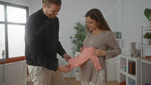 Wallpaper Mural Pregnant woman and man prepare nursery in baby room with crib, displaying new pink baby clothes in a cozy home setting, emphasizing family bonding and anticipation. Torontodigital.ca