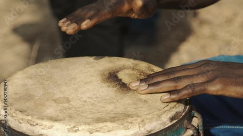 Slow motion close-up of woman’s hands playing traditional djembé drum during celebration in Senegal, with rhythmic finger movement and cultural expression in festive outdoor atmosphere