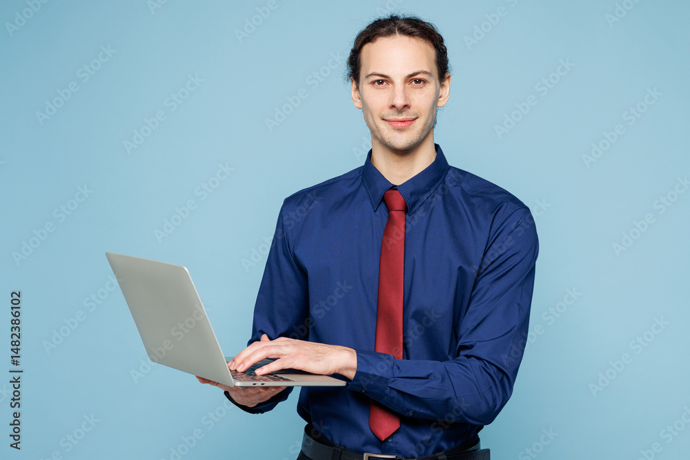 Young employee IT business man corporate lawyer he wears classic formal shirt red tie work in office hold use laptop pc computer look camera isolated on plain pastel blue background studio portrait. Young employee IT business man corporate lawyer he wears classic formal shirt red tie work in office hold use laptop pc computer look camera isolated on plain pastel blue background studio portrait.