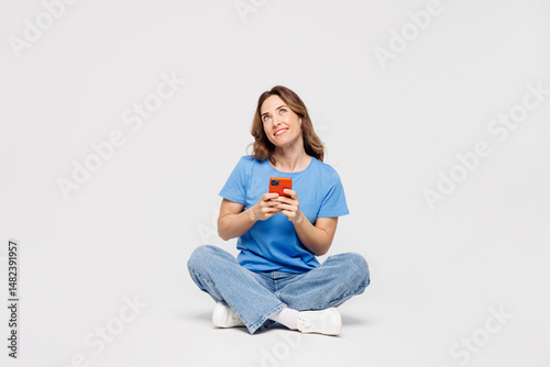 Εκτύπωση καμβά Full body young minded woman wears blue t-shirt casual clothes sit hold in hand use mobile cell phone look overhead isolated on plain solid white color background studio portrait