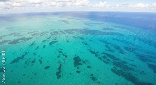 Aerial view of vibrant turquoise ocean with coral reefs and clouds above