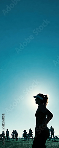 A silhouetted female coach watches her team practice as the sun sets, embodying leadership and determination in the dynamic world of youth football.
