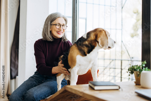 Картината върху платно Senior woman petting her beagle dog at home by the window