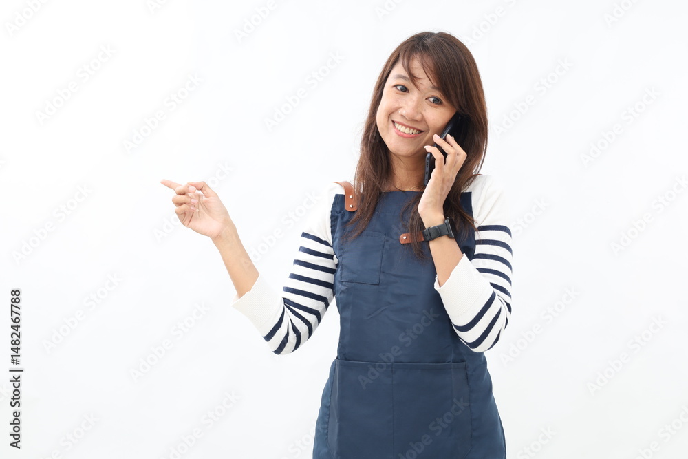 Young asian woman barista employee in blue apron work in coffee shop talk by mobile phone point finger aside on copy space isolated on white background. Small business startup Young asian woman barista employee in blue apron work in coffee shop talk by mobile phone point finger aside on copy space isolated on white background. Small business startup