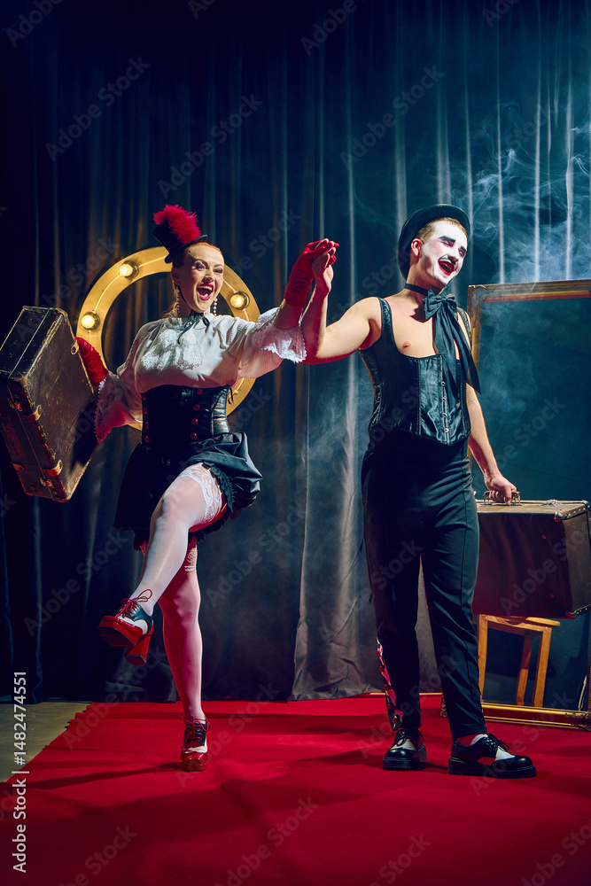 Fototapeta premium Joyful cabaret couple walks forward holding hands smiling in red gloves and hat with suitcases. Concept of cabaret, retro, lifestyle, performance, humor, show, celebration, theater, circus.