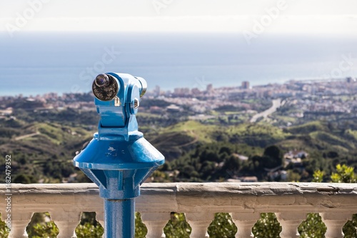 A bright blue coin-operated telescope overlooking the coastal landscape of Mijas, Málaga, Spain, with panoramic sea and city views under a clear daytime sky