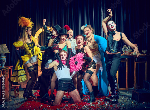 Cuadro en lienzo Cabaret cast laughs around central performer with pink boa and hats under spotlight on confetti carpet