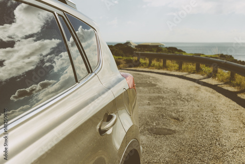 Close up of bronze coloured car parked on side of road with sky and clouds reflected in the window