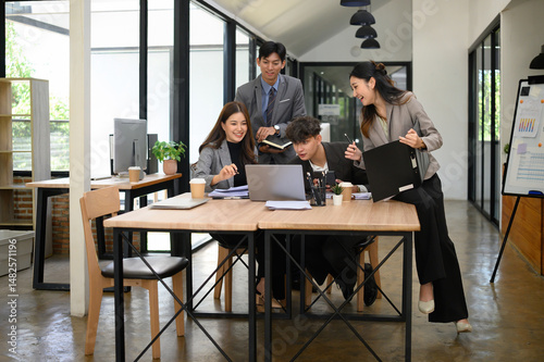 Group of young business professionals engaged in a lively brainstorming session around a laptop in a modern office