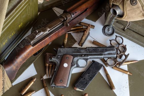 Gun and a lot of bullets are on a table. The gun is a rifle and the bullets are in a pile