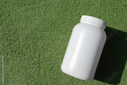 
A close-up shot of a white supplement bottle resting on a patch of vibrant green grass.