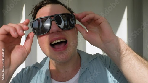 A sunbeam blinds a man in the eyes. Puts sunglasses on his head. Squints from the bright sun. Slow motion