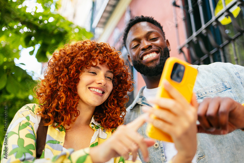 Two happy tourists are using a smartphone and smiling outdoors