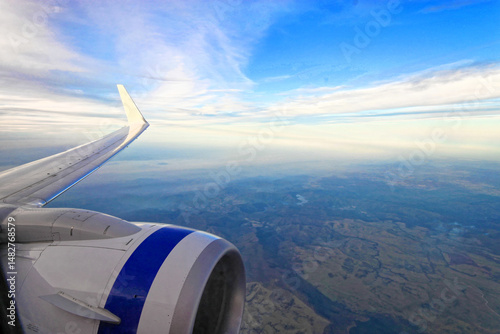 Wing and engine of aeroplane with blue sky and earth below - copy space