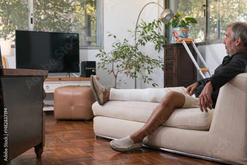 Senior man resting with broken leg watching television at home