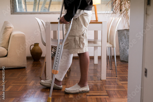 Man walking with crutches and leg in plaster cast at home