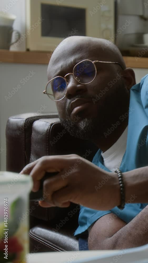 Vertical shot of sleepy clinician in medical scrubs napping on couch in break room, taking mobile gadget from table, getting up and hurrying to sick patient