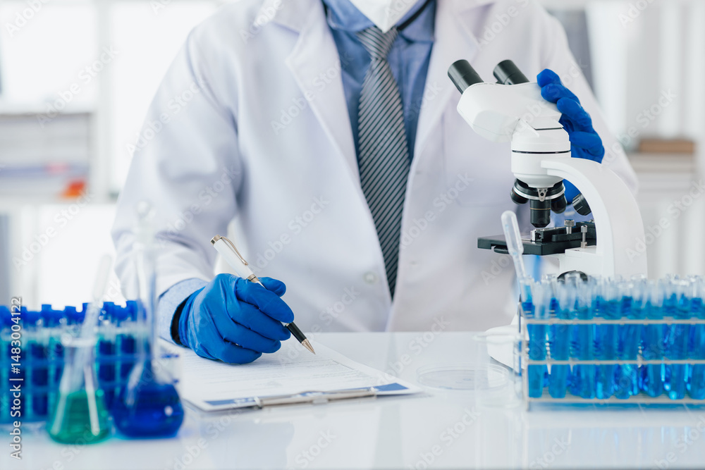Fototapeta premium Scientist taking notes during experiment in laboratory. The lab table is filled with test tubes, beakers, and a microscope.