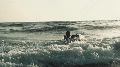African surfer's ocean dive: slow motion entry into Cap Skirring sea, golden hour swimming with surfboard, Casamance coastline