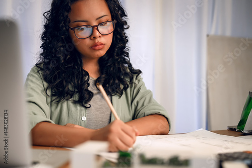 Young female student wearing glasses is focused on writing or drawing a project at her desk at night.