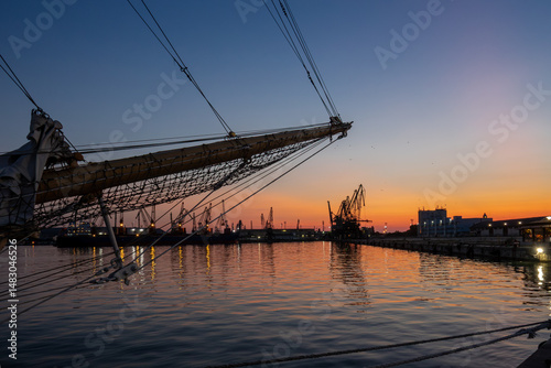 Tall ship silhouette in harbor at sunset. Scenic maritime evening view, travel destination.