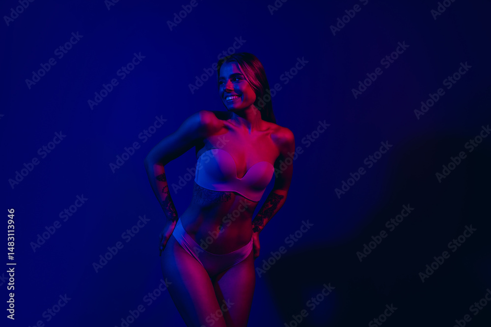 Obraz premium Fashionable young woman posing in neon light, showcasing style and confidence, with a vibrant and glowing blue background