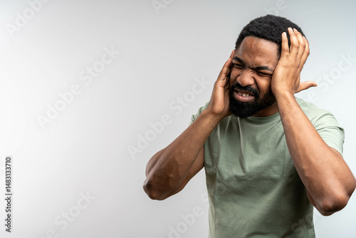 Portrait of young aArican American man isolated on gray background, suffering from severe headache, pressing fingers to temples with closed eyes
