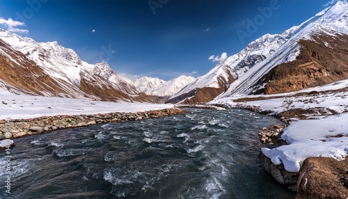 Close-up shot of the Chandra River flowing through a snow-covered Himalayan mountain range in winter, as seen from Gondhla village in Lahaul and Spiti district