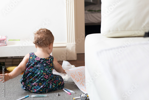 A cute toddler sits on the floor, engrossed in drawing with colorful markers.