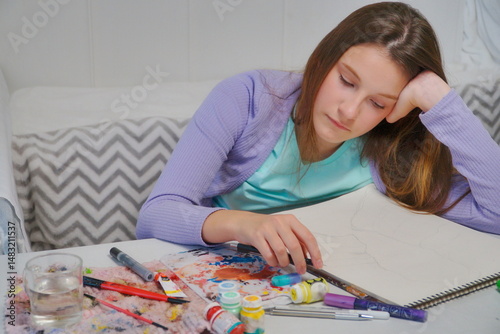 Little girl thinking and starting to paint with acrylics at the desk