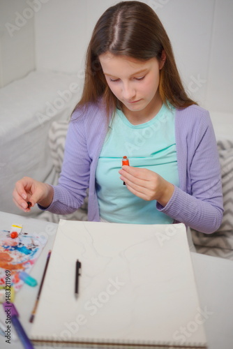 Little girl thinking and starting to paint with acrylics at the table