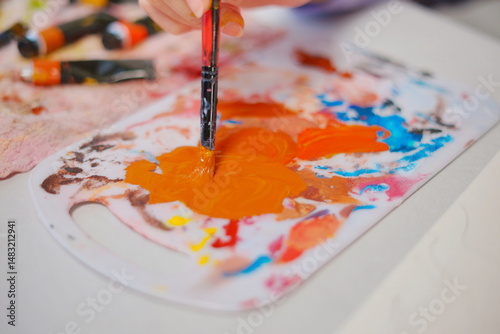 Close-up of a little girl hand mixing paint with a brush on a palette