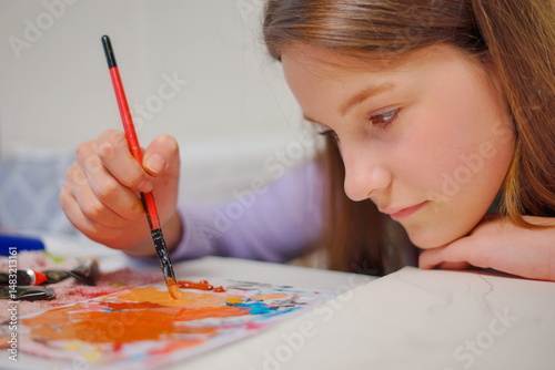 Close-up of a little girl hand mixing paint with a brush on a palette