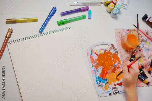 Close-up top view of a little girl starting to paint with acrylics in a sketchbook