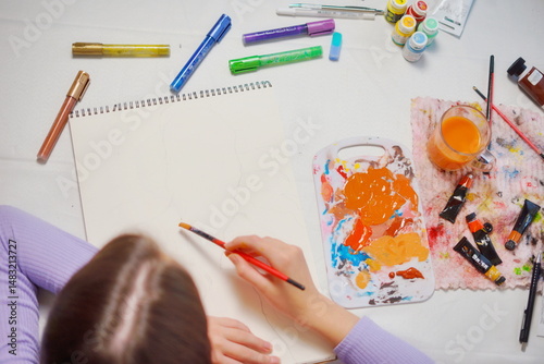 Close-up top view of a little girl starting to paint with acrylics in a sketchbook