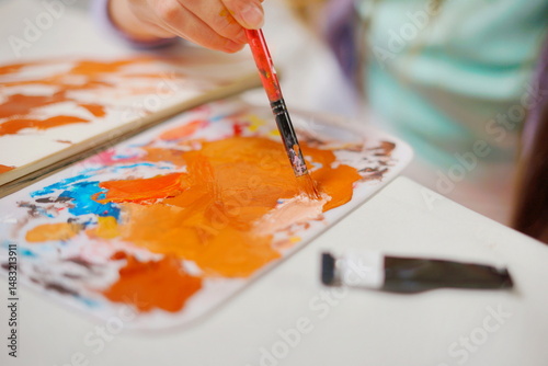 Close-up of a little girl hand mixing paint with a brush on a palette