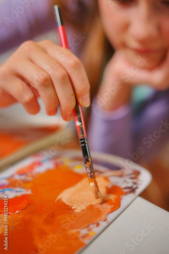 Close-up of a little girl mixing paints with a brush on a palette