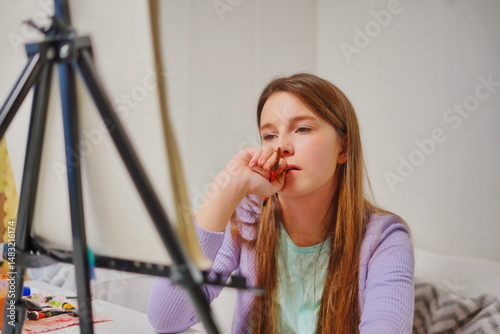 Close-up of a little girl with long brown hair sitting at a desk with an easel