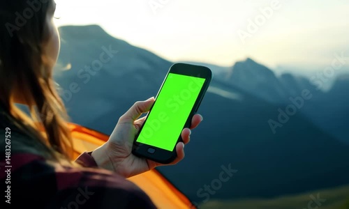 Tech Explorer: A woman using a smart phone with a green screen on a camping adventure, offering space for any digital experience amid nature's grandeur.
