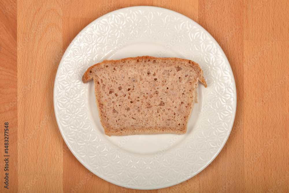 Slice of breadA single slice of light brown, porous bread rests on a white, patterned plate set against a light brown wooden surface