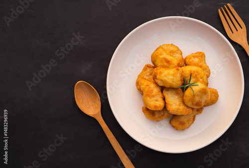 Top view of crispy fried chicken nuggets and rosemary in white plate on black table background.