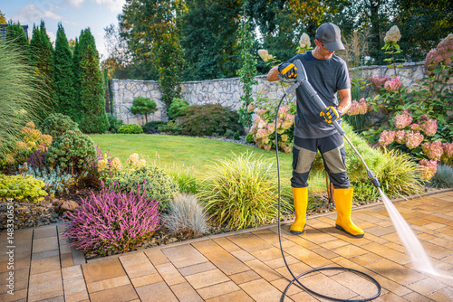 Gardener Uses Pressure Washer to Clean Patio in Lush Garden During Sunny Afternoon