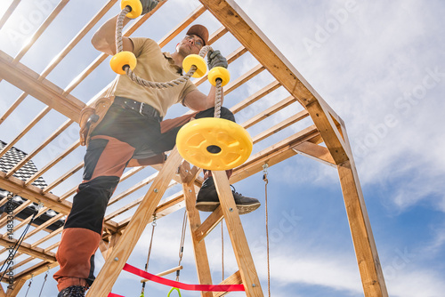 Canvas Print Construction of a Wooden Playground Structure With a Man Installing Yellow Rope